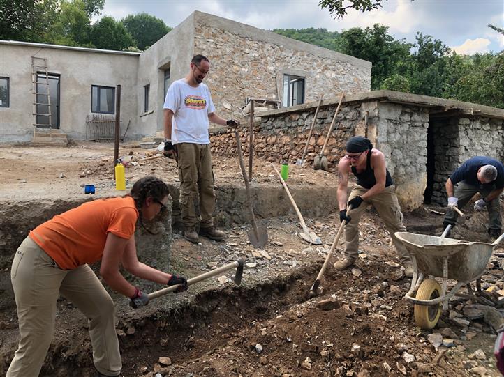 A group of people are digging in the dirt in front of a stone building.