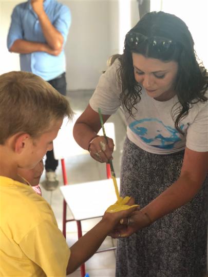 A woman is painting a child 's face with a yellow brush