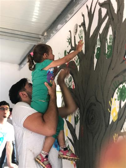 A man is holding a little girl who is trying to paint a tree on a wall