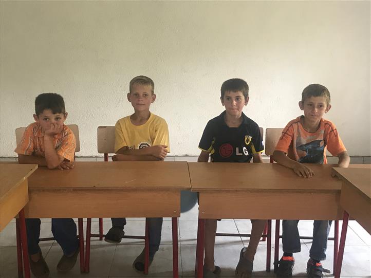 Four young boys are sitting at desks in a classroom.