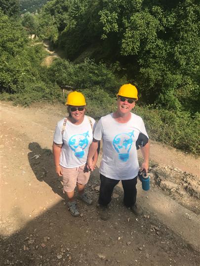 Two people wearing hard hats and sunglasses are standing next to each other on a dirt road.