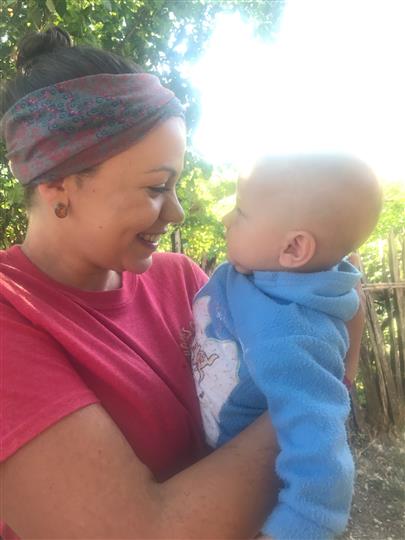 A woman in a red shirt is holding a baby in her arms.