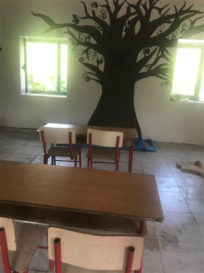 A classroom with tables and chairs and a tree painted on the wall