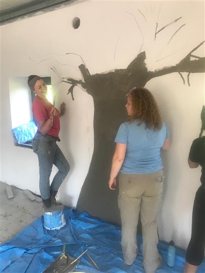 Two women are painting a tree on a wall