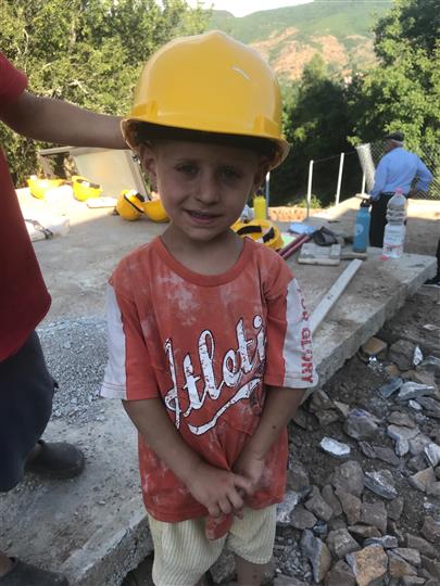 A little boy wearing a yellow hard hat and an orange shirt