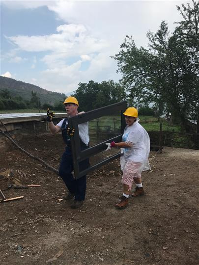 A man and a woman wearing hard hats are carrying a large piece of wood.