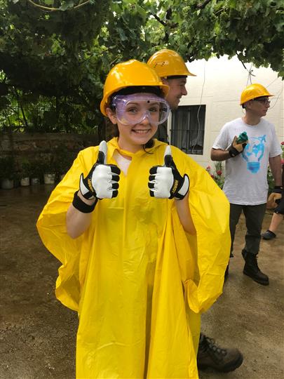 A girl wearing a yellow raincoat and hard hat is giving a thumbs up