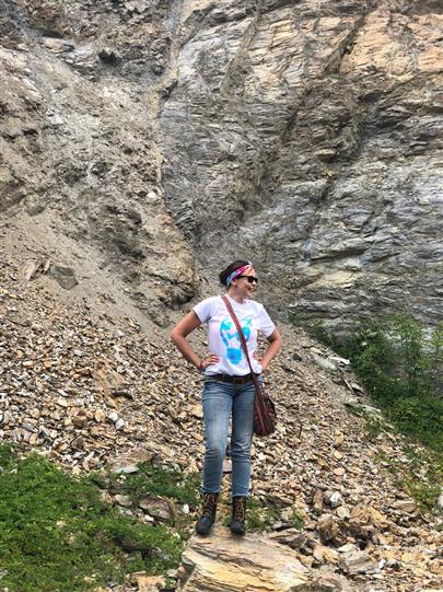 A woman is standing on a rocky hillside with her hands on her hips.