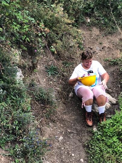 A woman is sitting on a rock in the woods holding a yellow bowl.