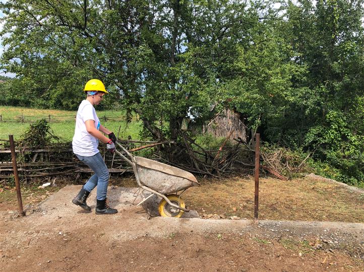 A man wearing a hard hat is pushing a wheelbarrow.