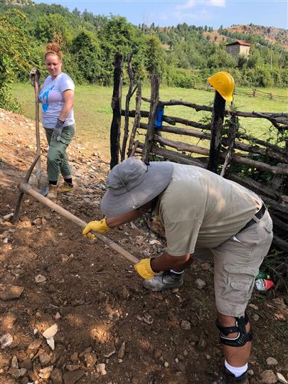 A man wearing a hat is digging in the dirt with a shovel.