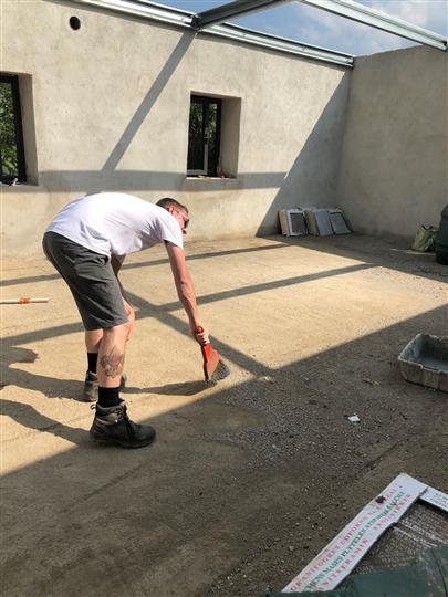 A man is bending over to brush the floor with a broom.