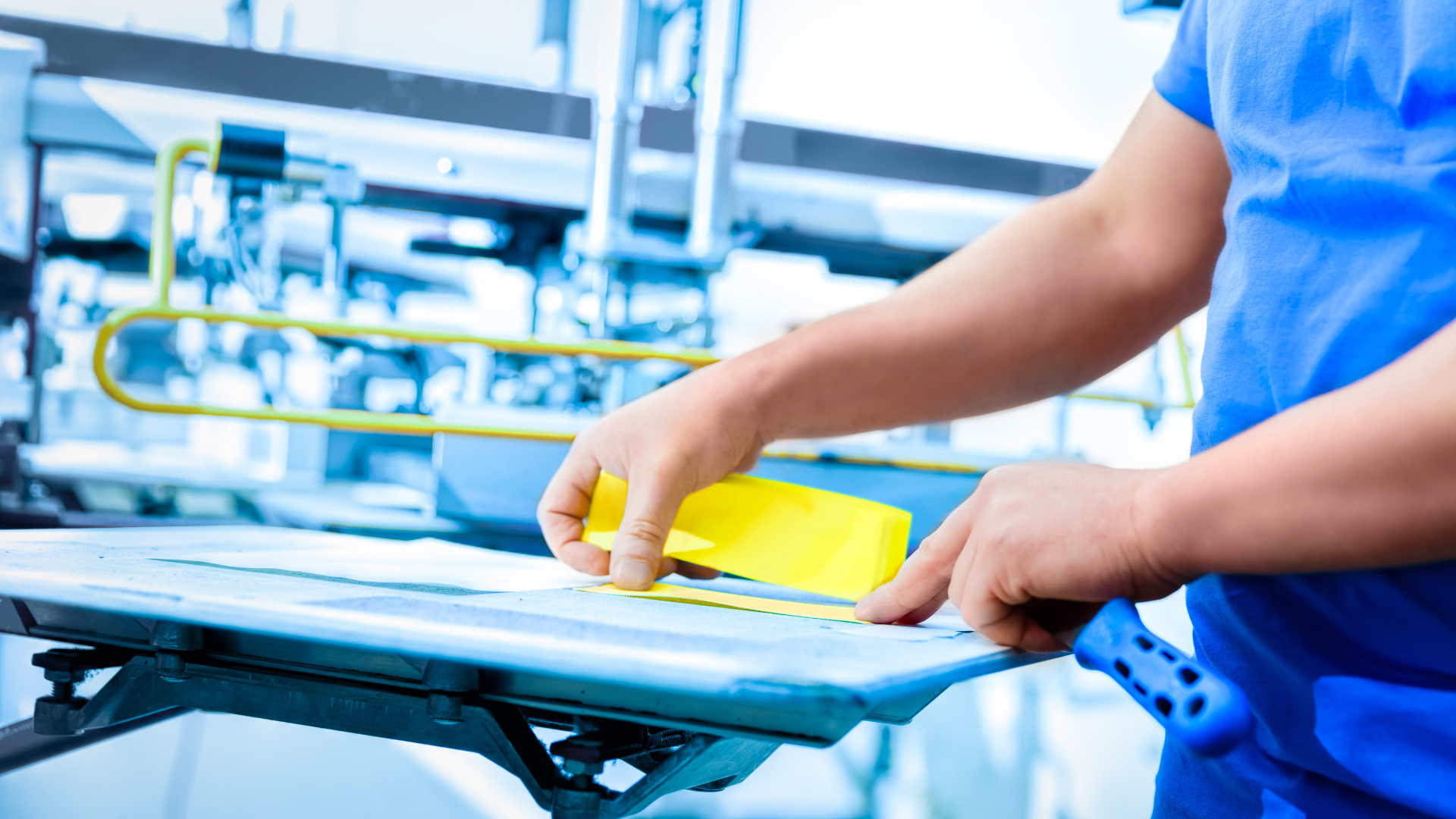 A man in a blue shirt is cutting a piece of yellow tape.