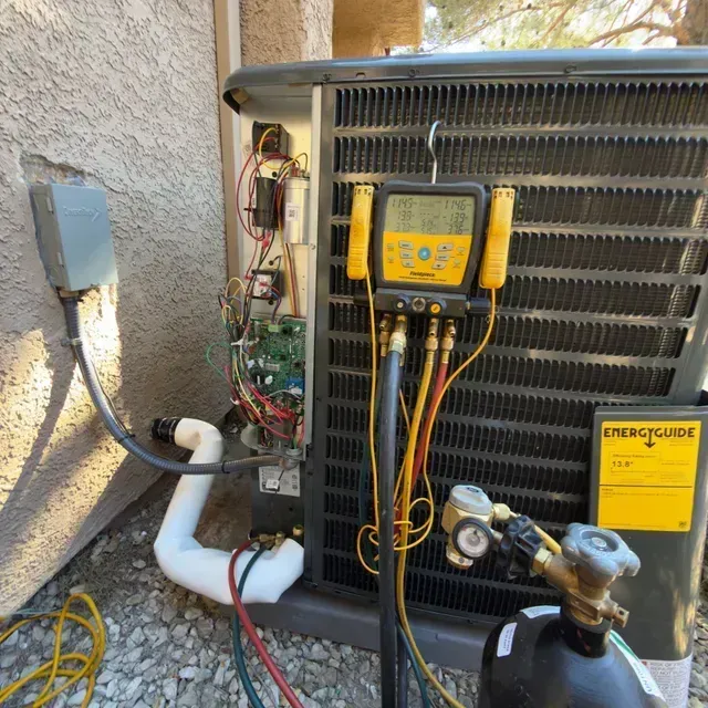 Outdoor HVAC condenser with gauges and exposed wiring beside a stucco wall