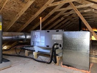 Furnace and ductwork installed in an unfinished attic with exposed wooden rafters.