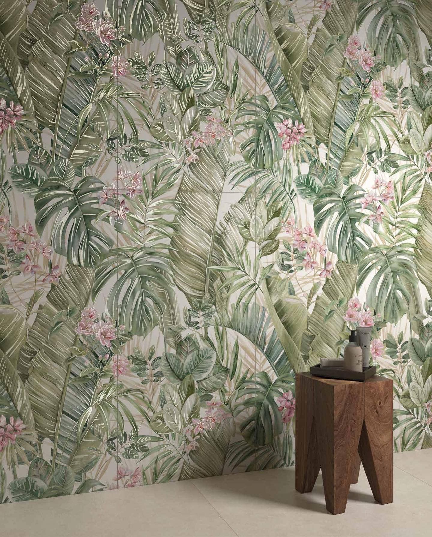 Carta da parati con foglie tropicali e fiori rosa, accanto a un piccolo sgabello di legno con vasi.