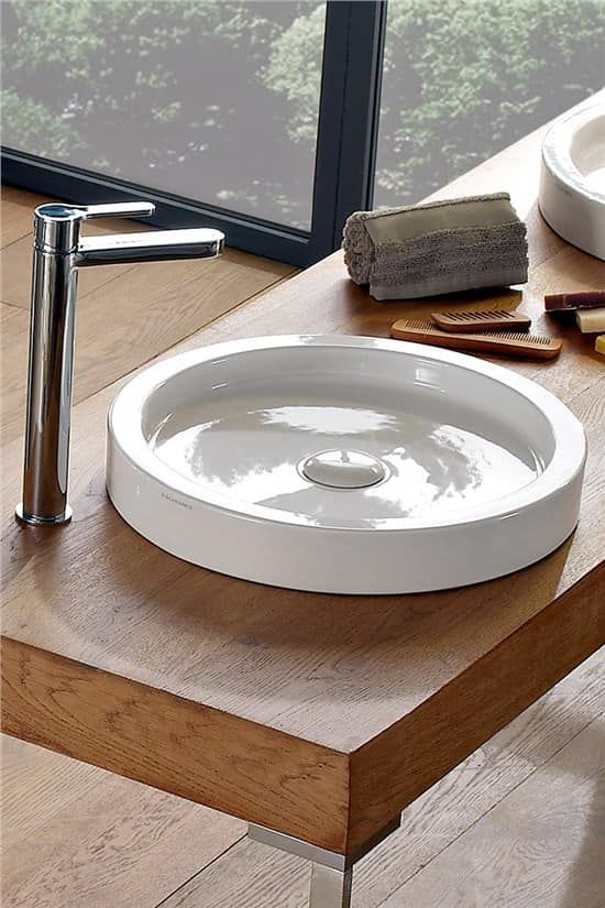 Lavandino rotondo bianco su piano di lavoro in legno con rubinetto cromato.