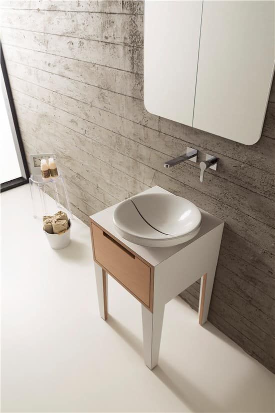 Mobiletto per il bagno con mobiletto bianco, cassetto in rame e lavandino rotondo su una parete in cemento strutturato.