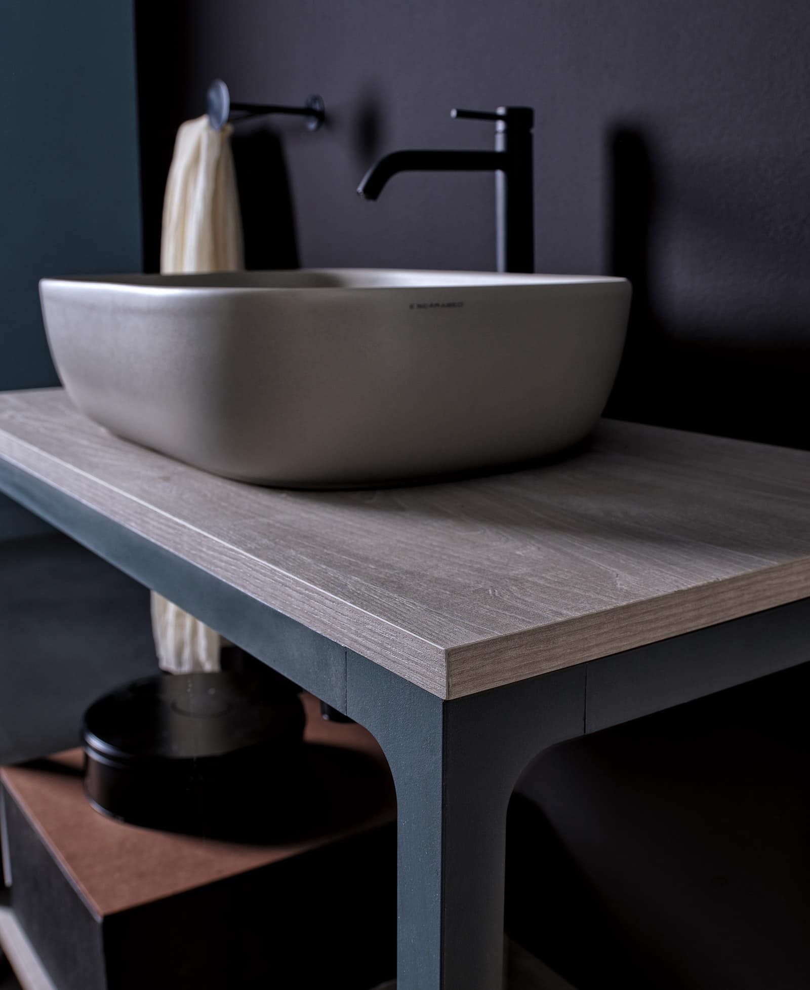 Mobile bagno con lavandino grigio effetto pietra e rubinetto nero su piano in legno. Pareti blu scuro.