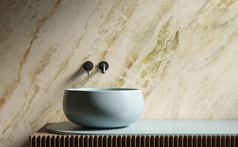 Lavabo azzurro su una superficie di legno, appoggiato su una parete effetto marmo con venature verdi e dorate.