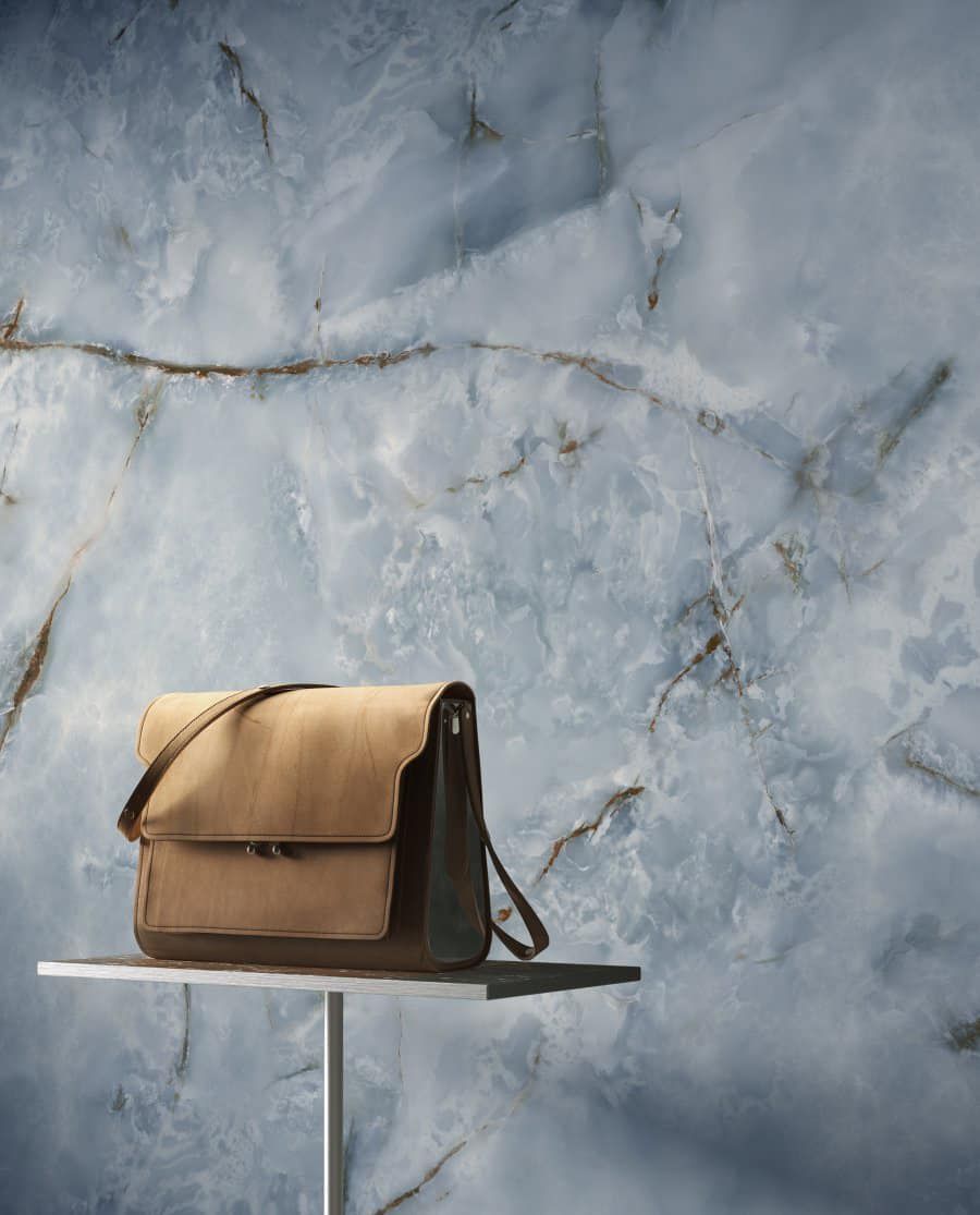 Borsa a tracolla in pelle marrone chiaro su un tavolino bianco, contro una parete in marmo blu con venature marroni.