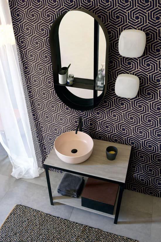 Mobile bagno con lavandino rosa, specchio ovale, carta da parati a fantasia e pavimento grigio.