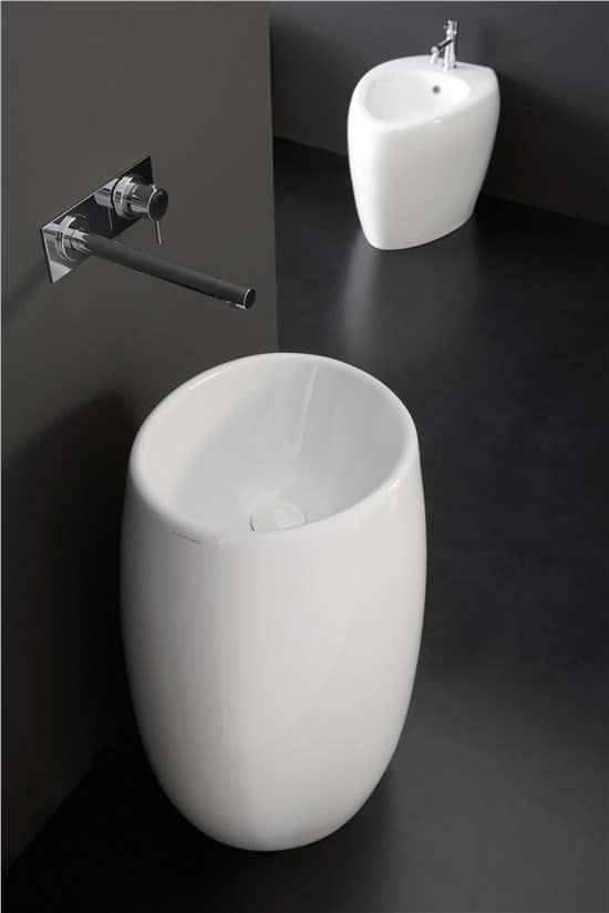 Bidet e lavandino bianchi di forma ovale in un bagno moderno con pavimento scuro e pareti grigie. Rubinetto a parete.