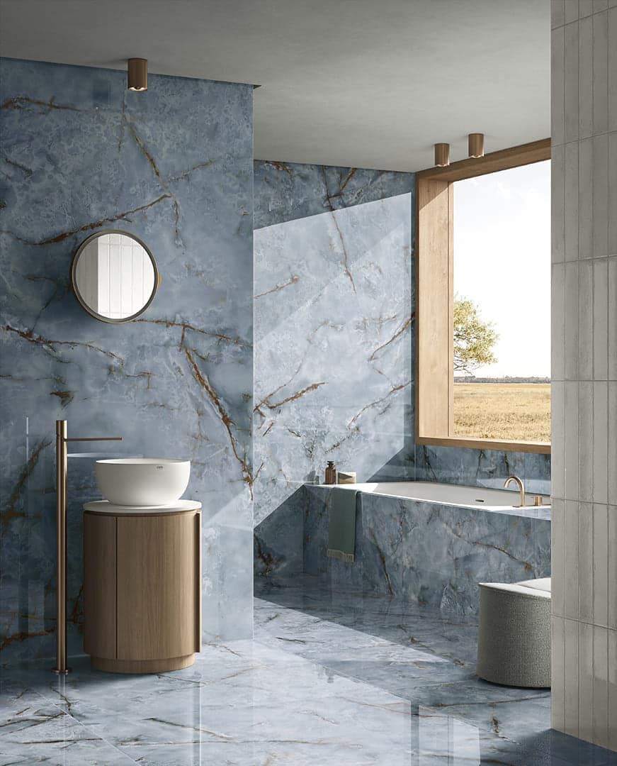 Bagno in marmo blu con specchio rotondo, mobile lavabo in legno e finestra con vista su un campo.