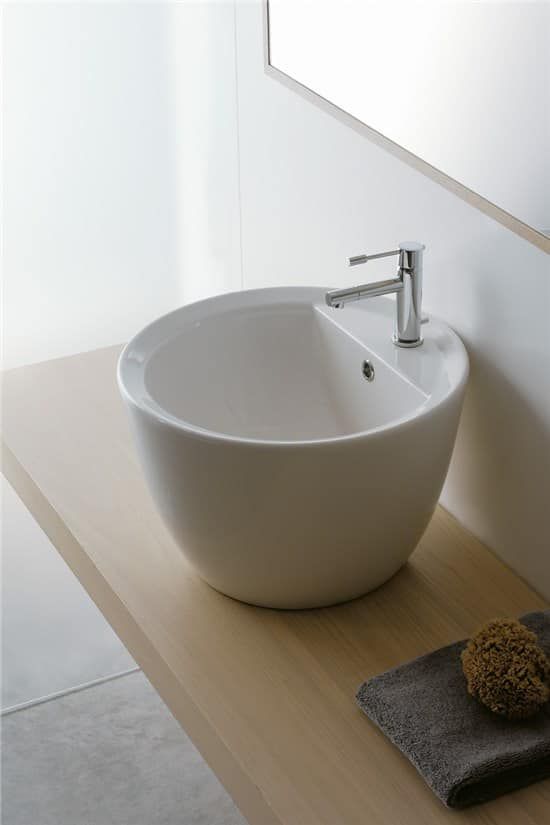 Lavandino in ceramica bianca su un piano in legno con rubinetto. Asciugamano e spugna grigi presenti.