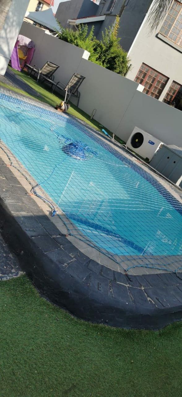 A rectangular swimming pool with blue water sits in a backyard with green artificial grass.
