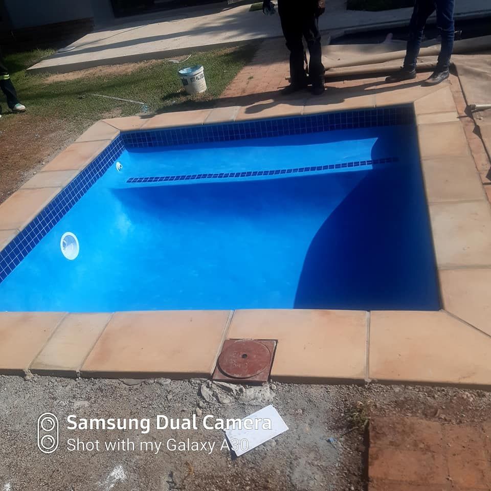 Blue rectangular pool with tiled edges and surrounding stone, people standing nearby.