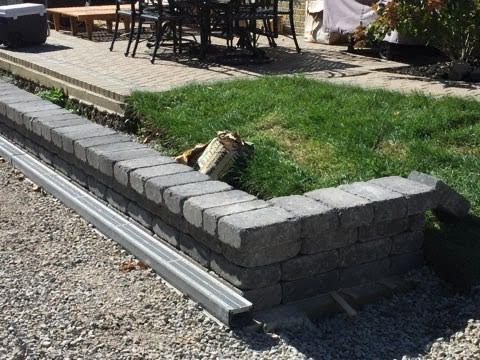 Stone retaining wall with a metal drainage channel. Grass and patio area in background.