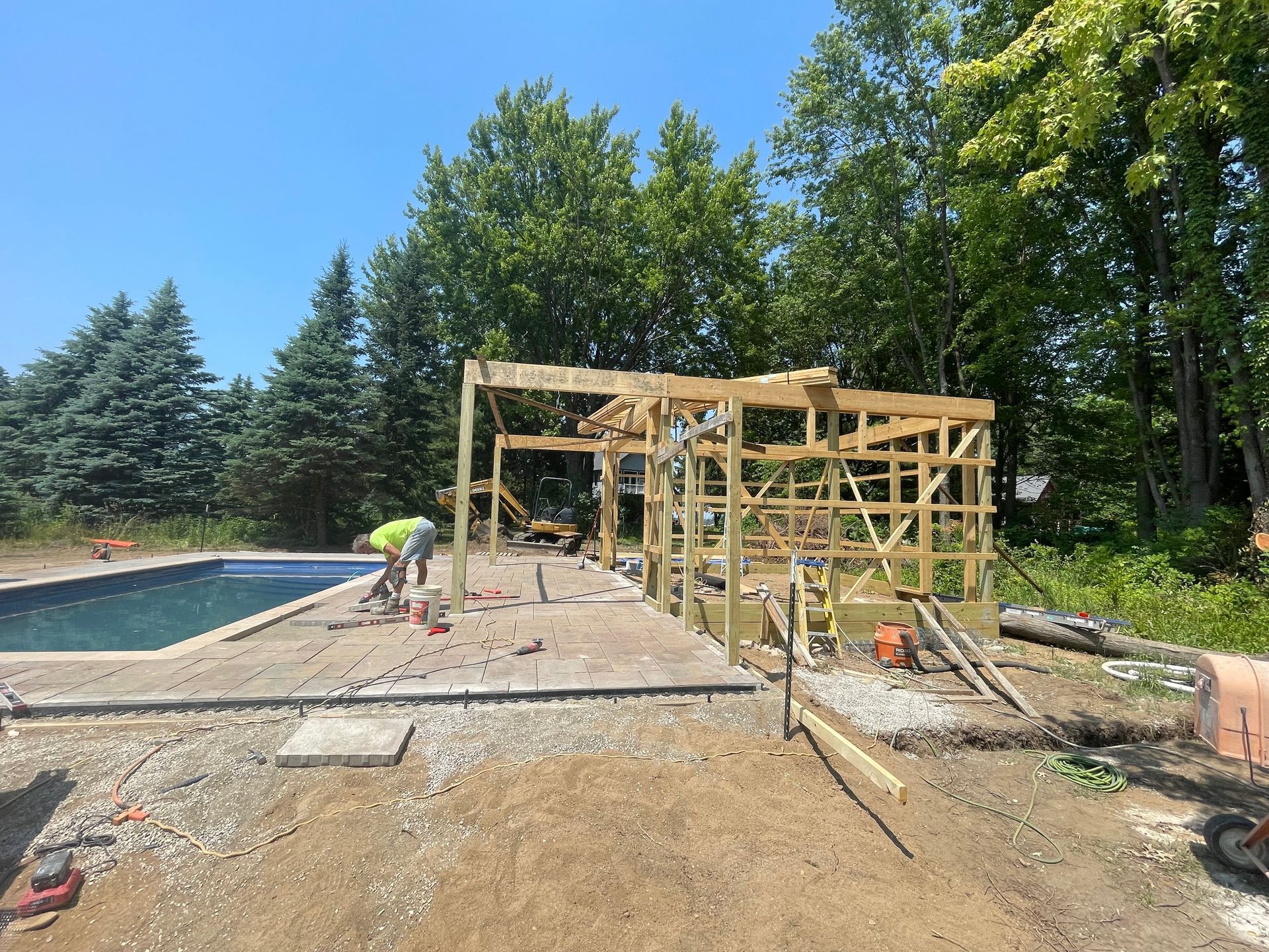 Construction of a wooden structure by a pool, worker visible, on a sunny day.