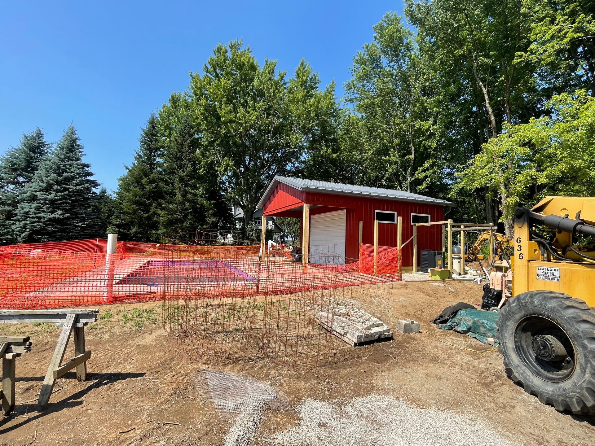 Red shed under construction behind a fence; a yellow skid steer is parked nearby.