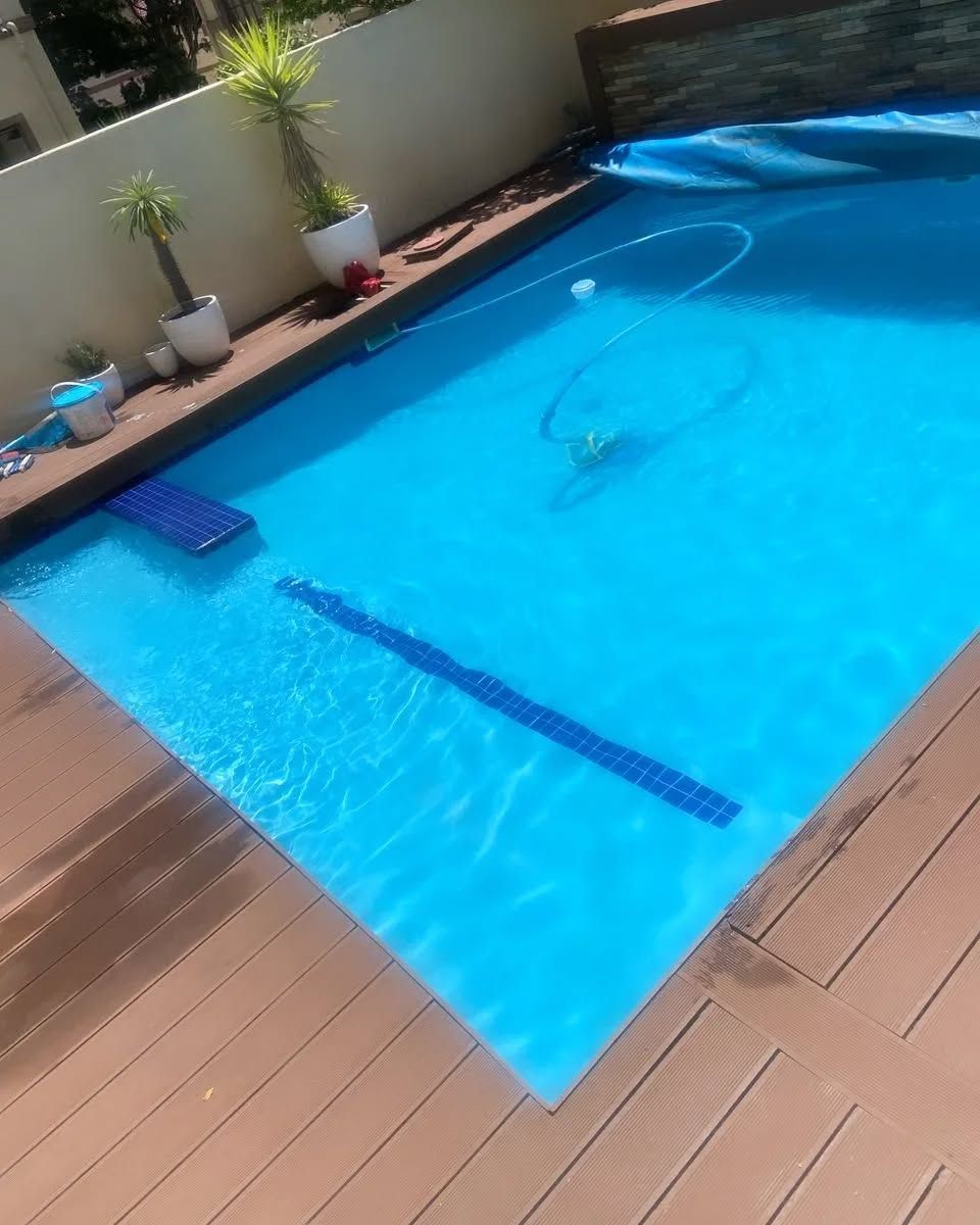 A rectangular swimming pool filled with blue water, surrounded by wooden decking.
