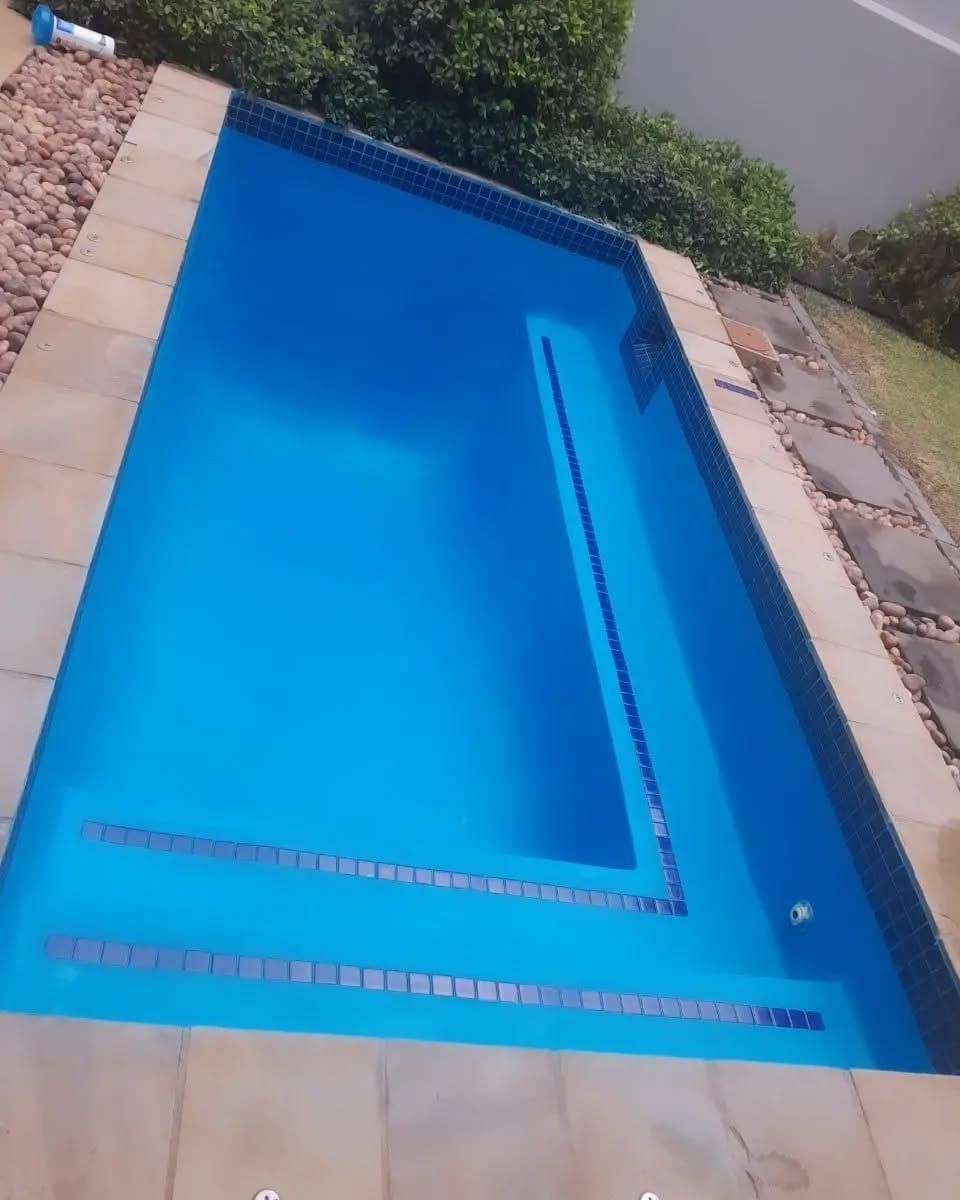 Blue rectangular swimming pool with steps, surrounded by stone and greenery.
