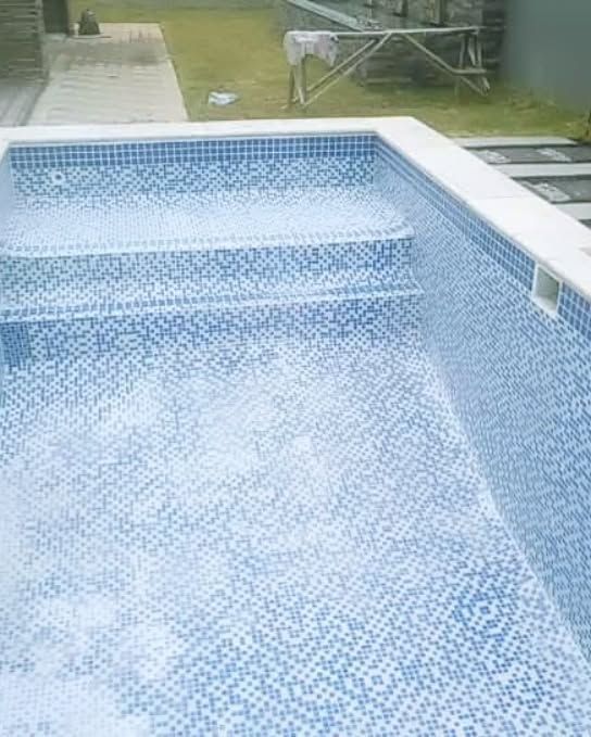 Empty swimming pool with blue tile interior and steps, outdoors.