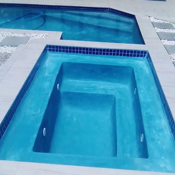 Blue-tiled hot tub and pool surrounded by white stone and pavers, outdoors.
