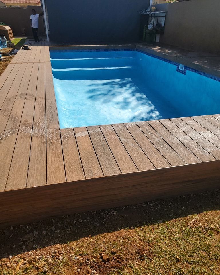 Pool with blue water and wooden decking; a person stands near the pool.