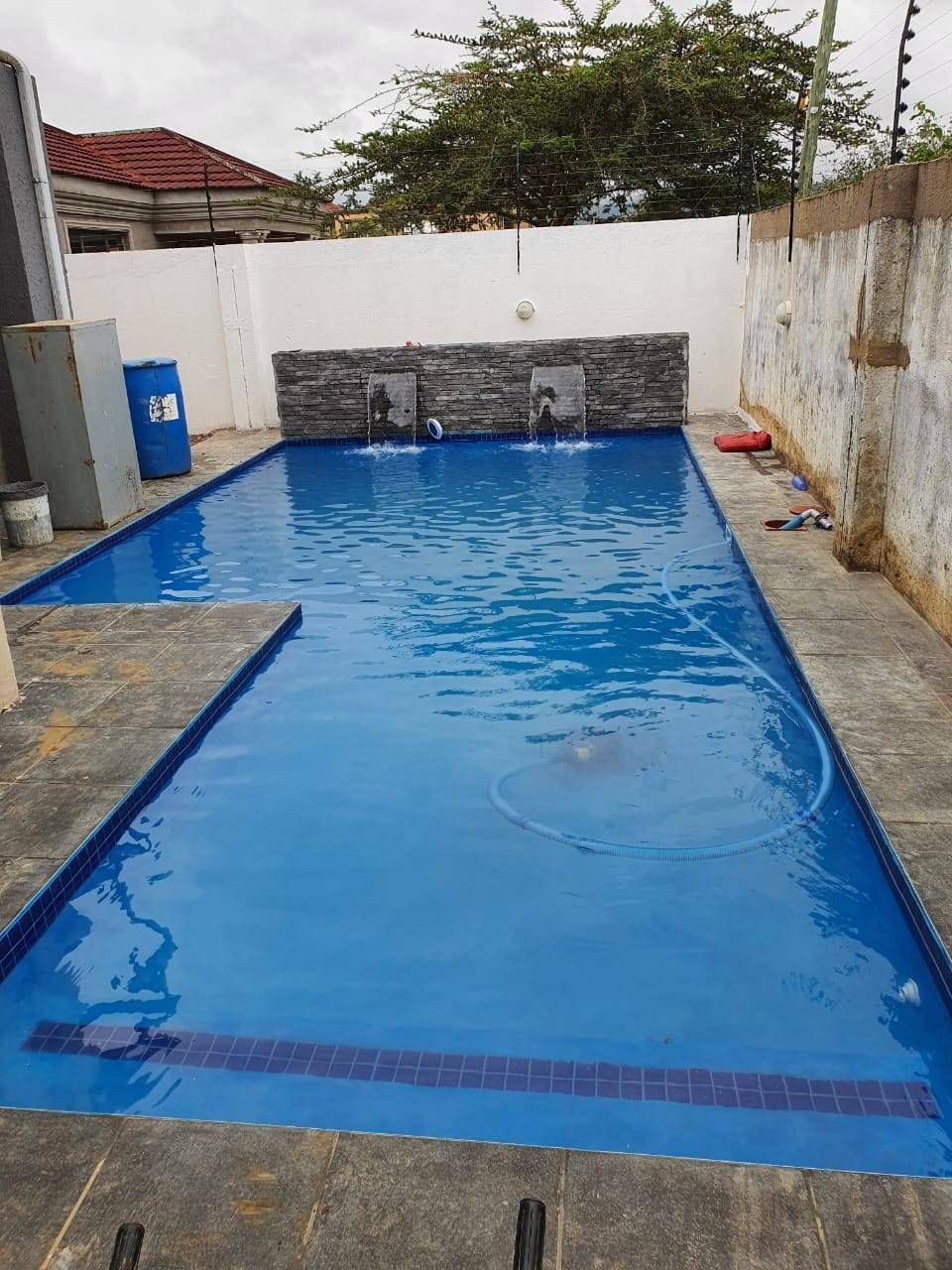 Blue tiled swimming pool with water fountains against a white and stone wall.