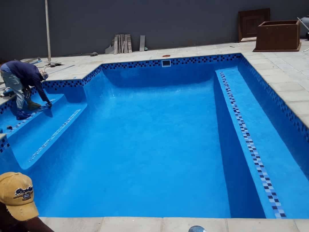 Person applying a blue sealant to an empty swimming pool. Dark blue tile border.