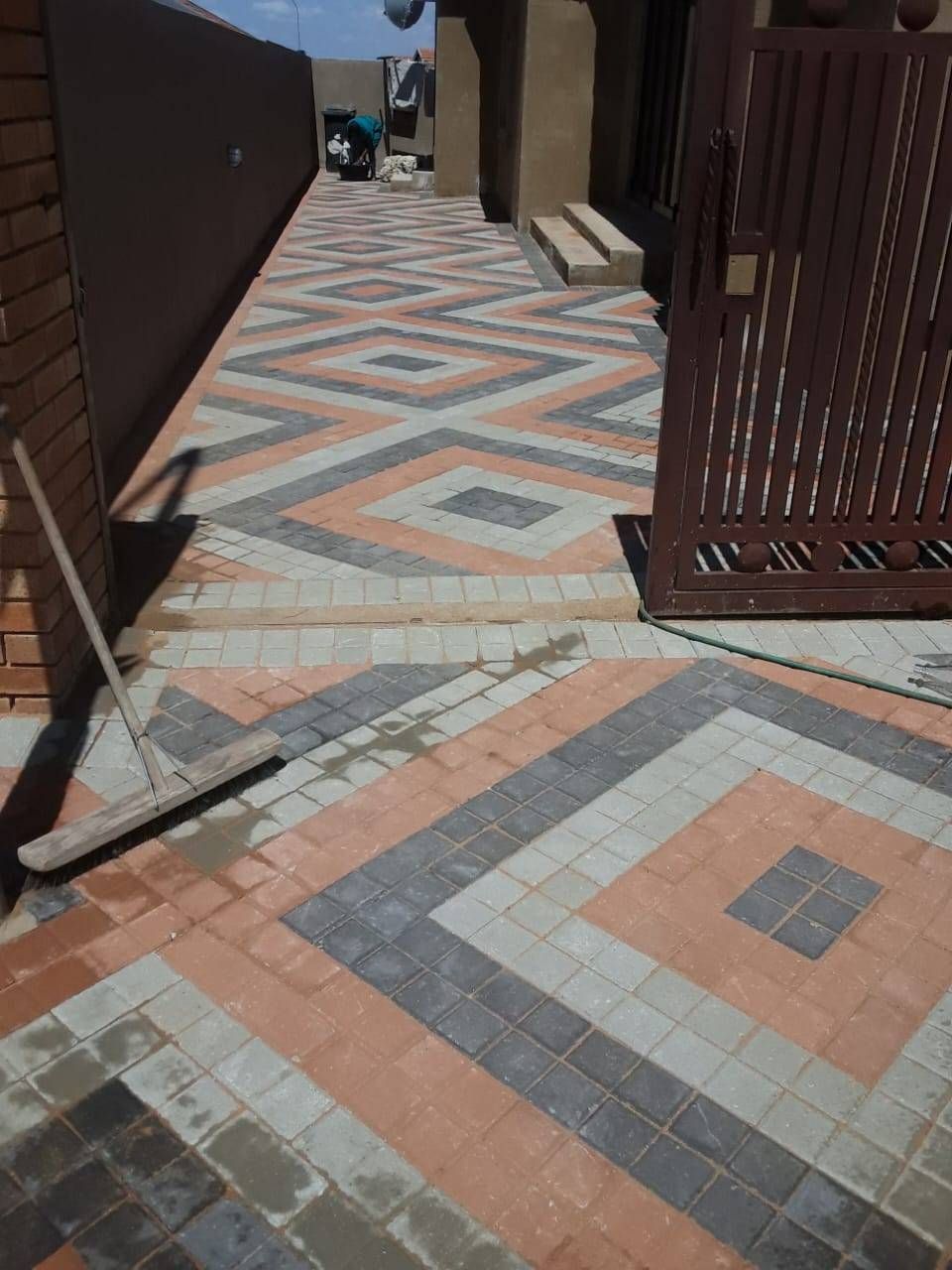 Brick paved walkway with diamond pattern in orange, gray, and white, leading to a doorway.