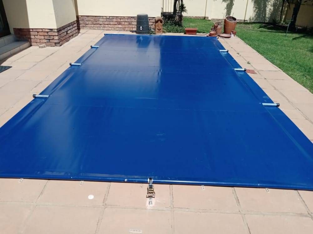 Blue pool cover stretched over a rectangular pool, secured with straps.