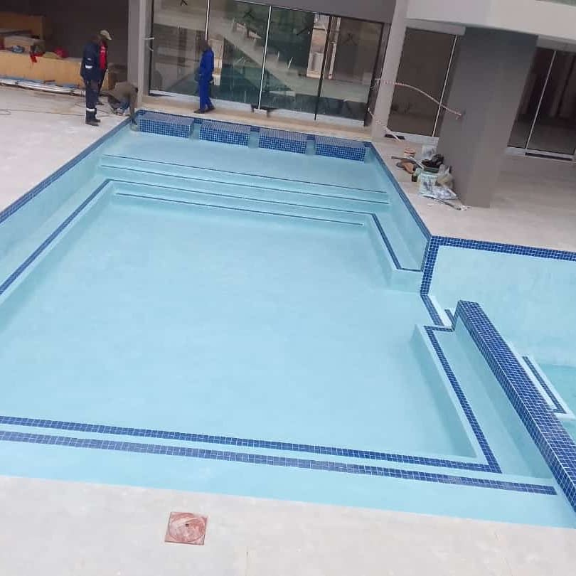 Newly constructed swimming pool with blue tiles and workers.