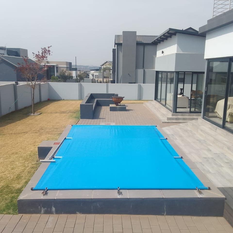 Blue pool cover on a rectangular pool in a backyard patio. A house is in the background.