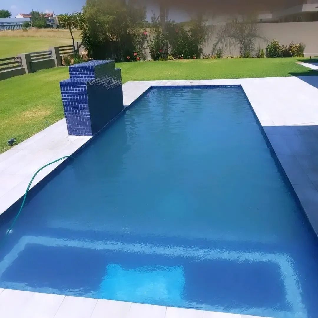 Rectangular blue swimming pool in a grassy yard, with blue tile feature and white paving.