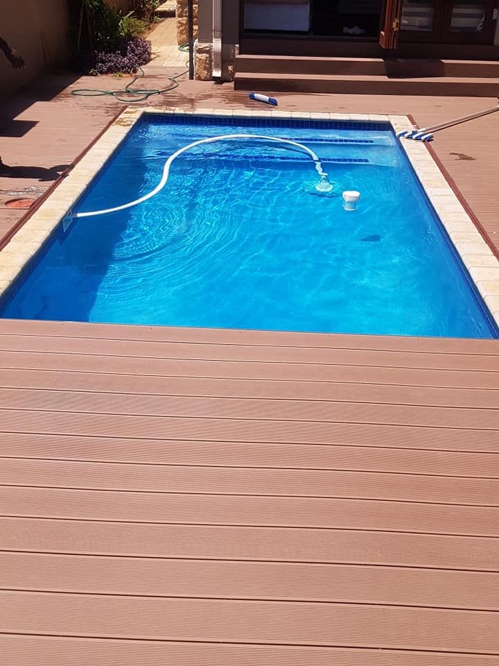 Rectangular blue swimming pool surrounded by brown composite decking. Pool equipment visible.