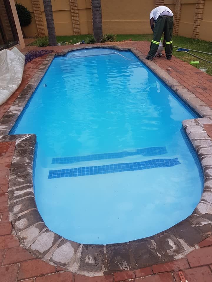 Swimming pool with blue water and brick surround; a person works nearby.