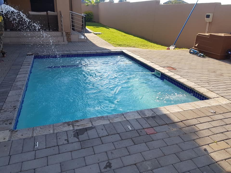 Rectangular pool with blue water, brick surround, water fountain, patio, and brown walls.