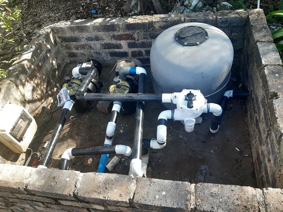 Pool filter system with pump, pipes, and tank in brick enclosure.